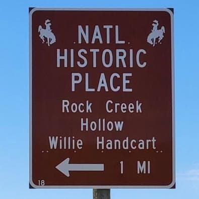 Brown highway sign: Natl Historic Place, Rock Creek Hollow, Willie Handcart, 1 mile, with arrow pointing left